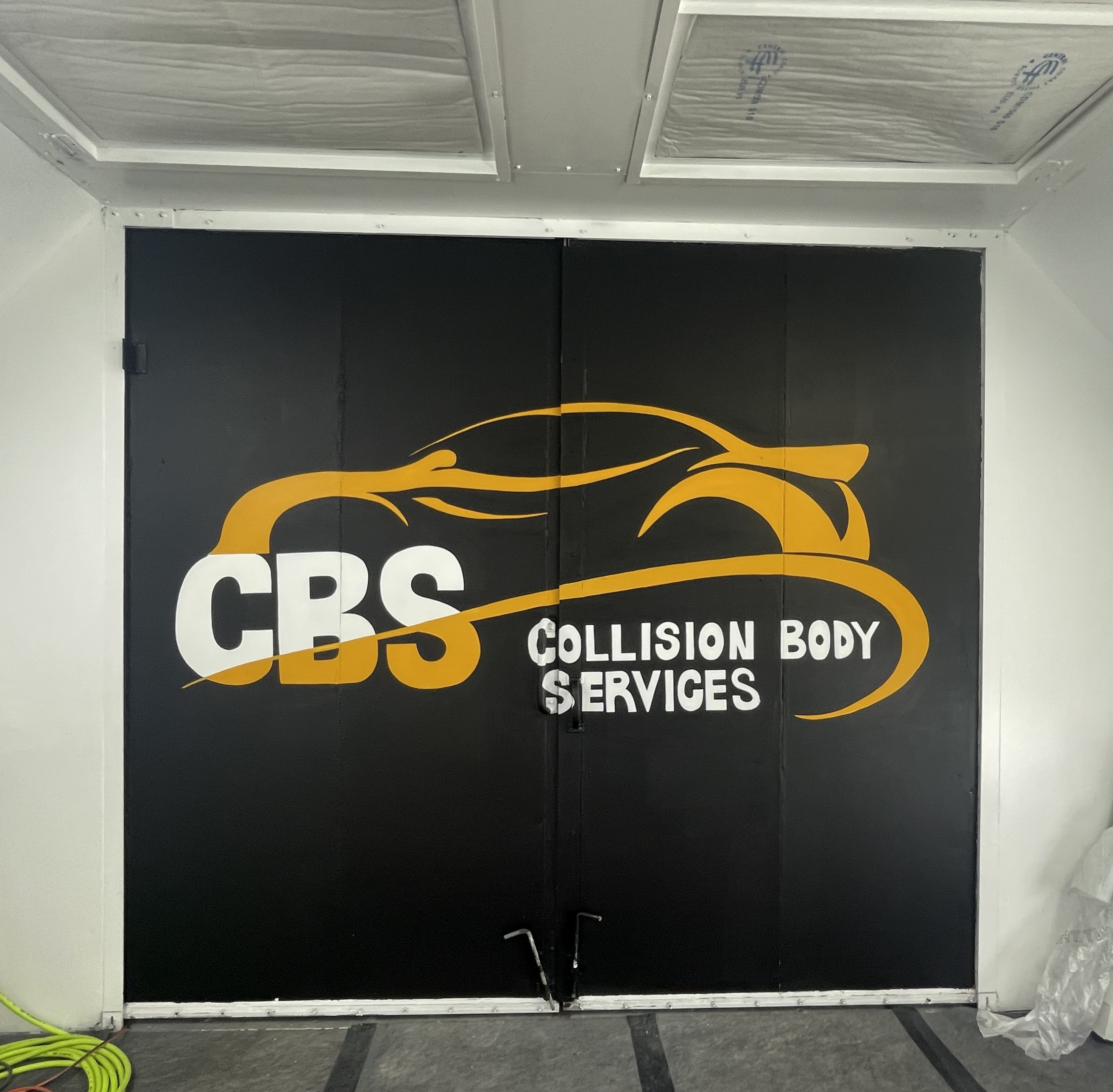 A hand-painted CBS Collision Body Services mural on large black doors.