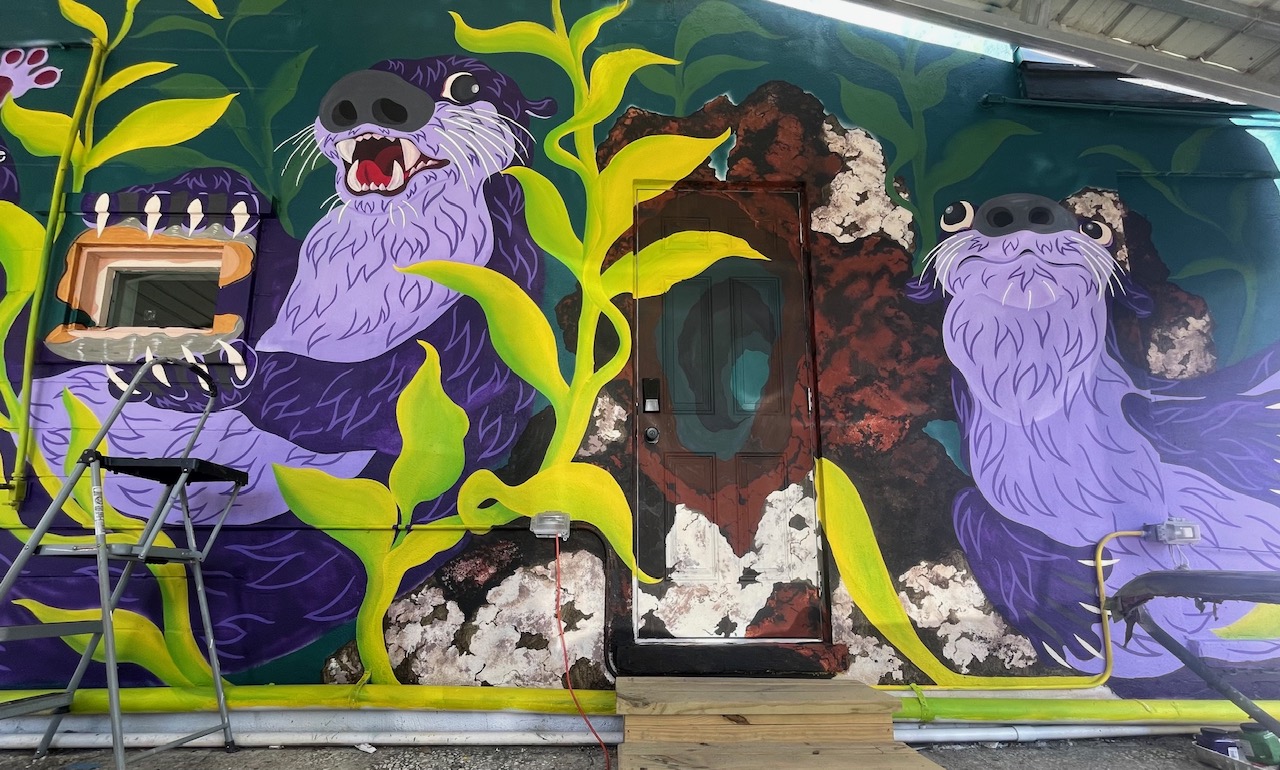 A colorful mural of playful purple otters surrounded by bright green leaves.